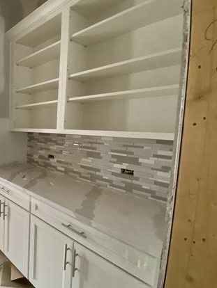 A kitchen with white cabinets , granite counter tops , and shelves.