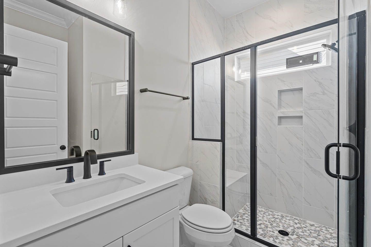 A bathroom with a toilet , sink , mirror and walk in shower.