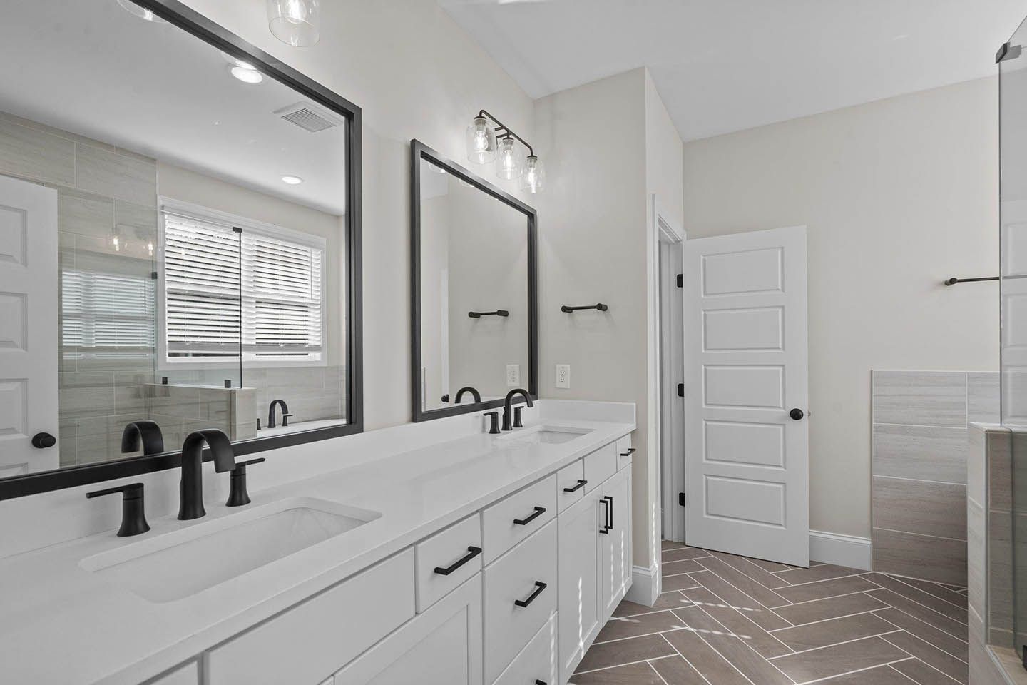 A bathroom with two sinks , two mirrors and a walk in shower.