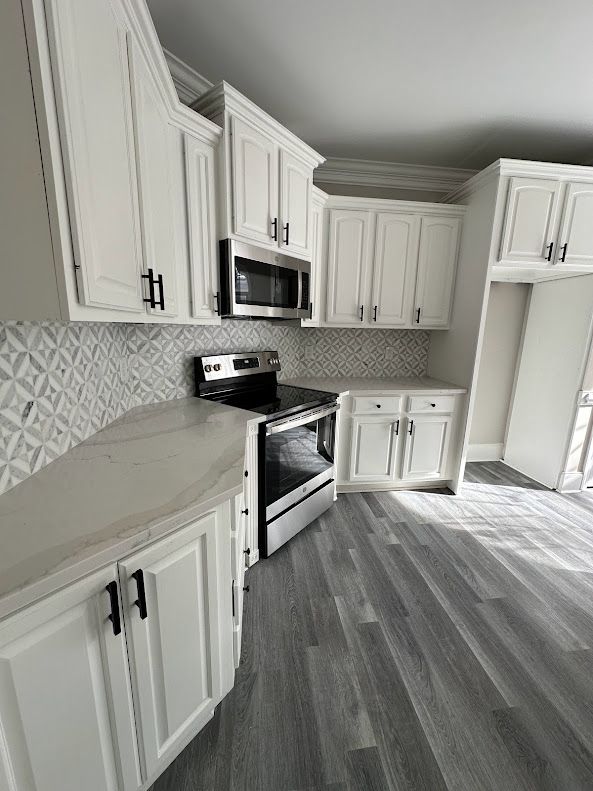 A kitchen with white cabinets , a stove , and a microwave.