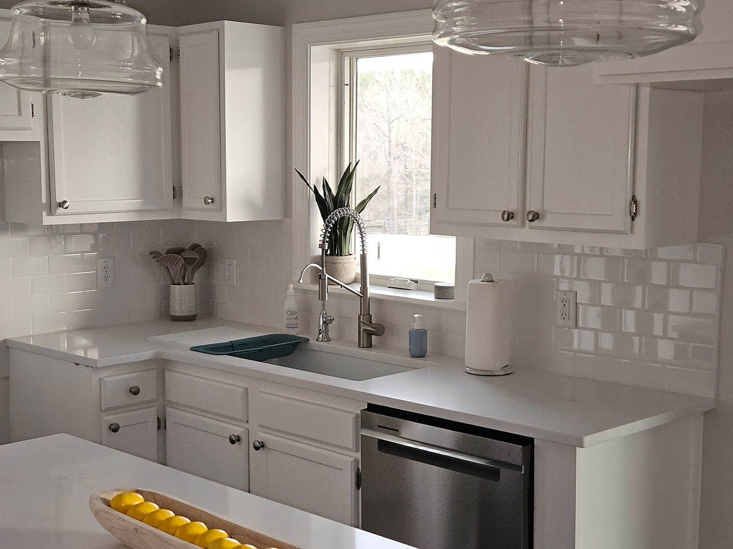 A kitchen with white cabinets , a sink , a dishwasher and a window.