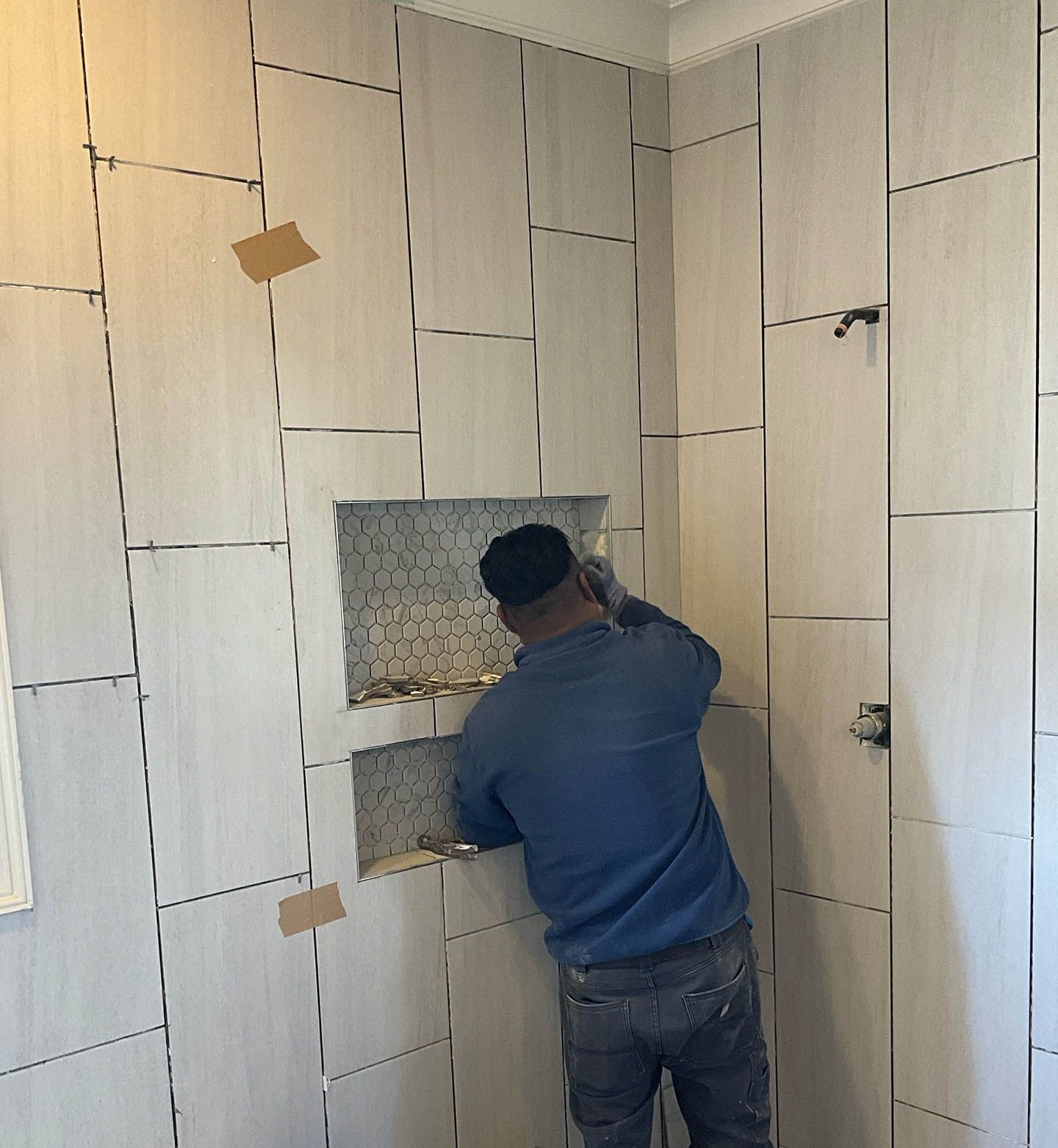 A man is working on a tiled wall in a bathroom.