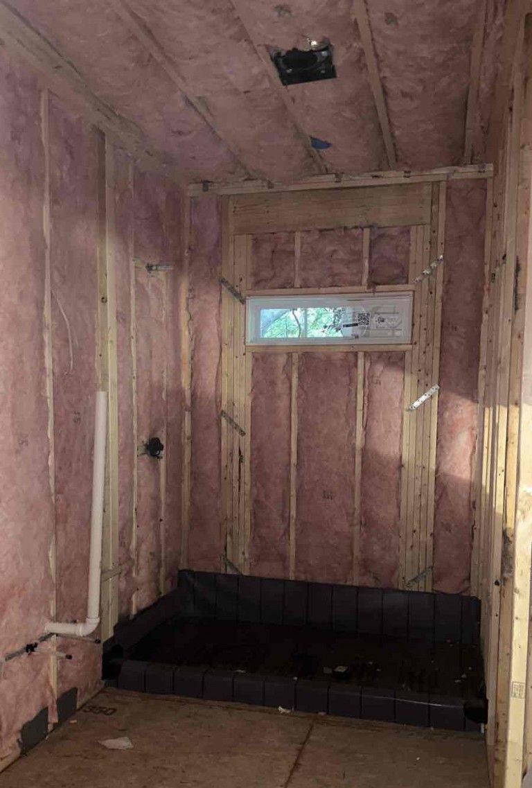A bathroom under construction with pink insulation and a window.
