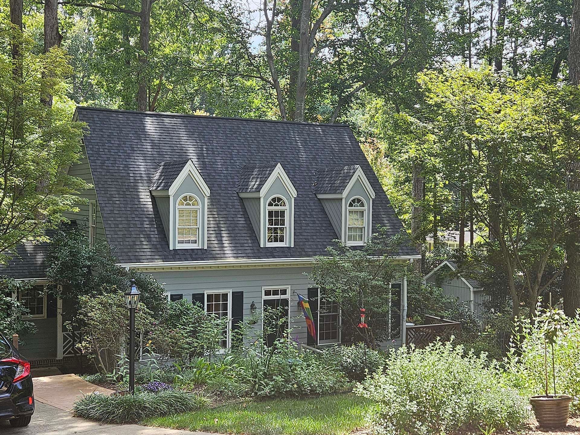 A house with a black roof and white trim is surrounded by trees.