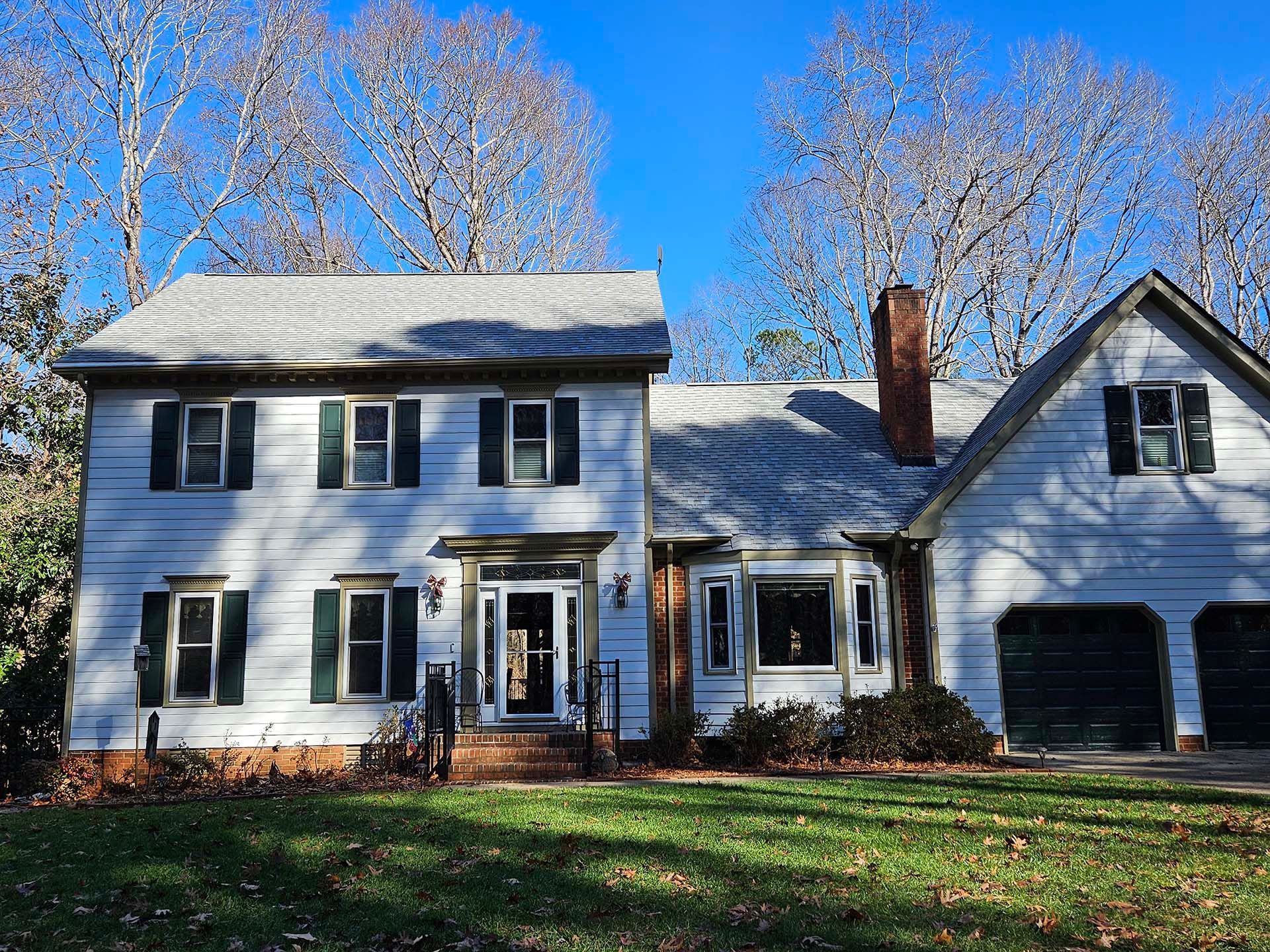 A large white house with black shutters is sitting on top of a lush green field.