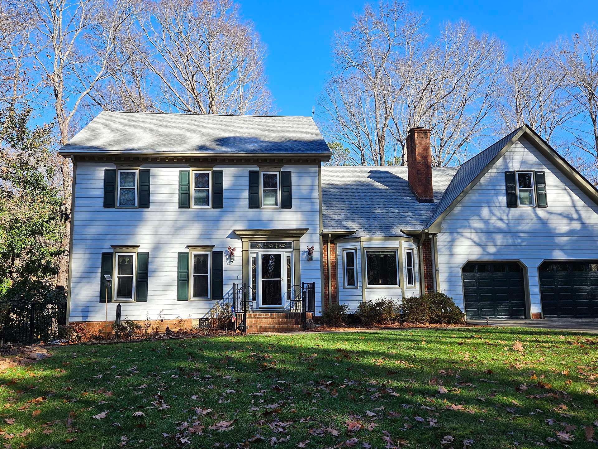 A large white house with green shutters is sitting on top of a lush green lawn.