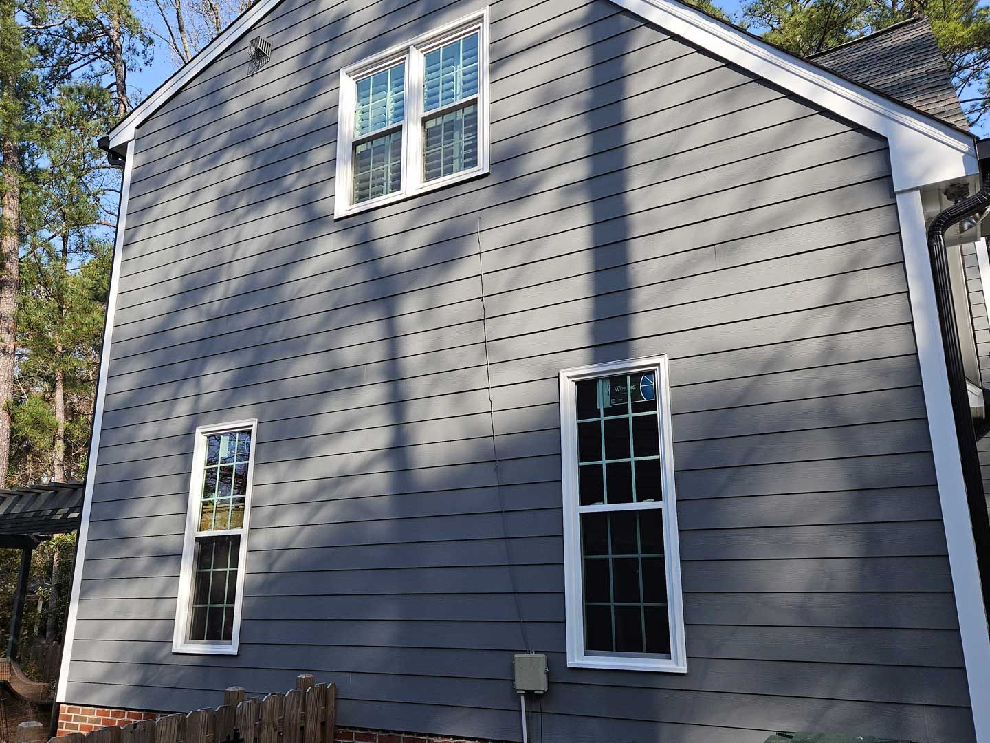The back of a house with a gray siding and white windows.