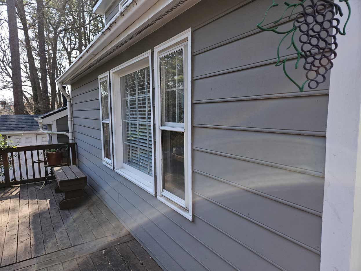 The side of a house with a gray siding and white windows.