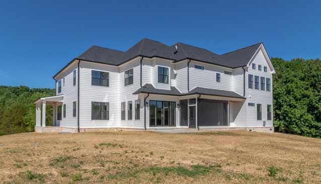 A large white house with a black roof is sitting on top of a grassy hill.