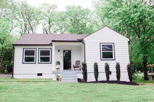 A small white house with a porch and trees in the background.