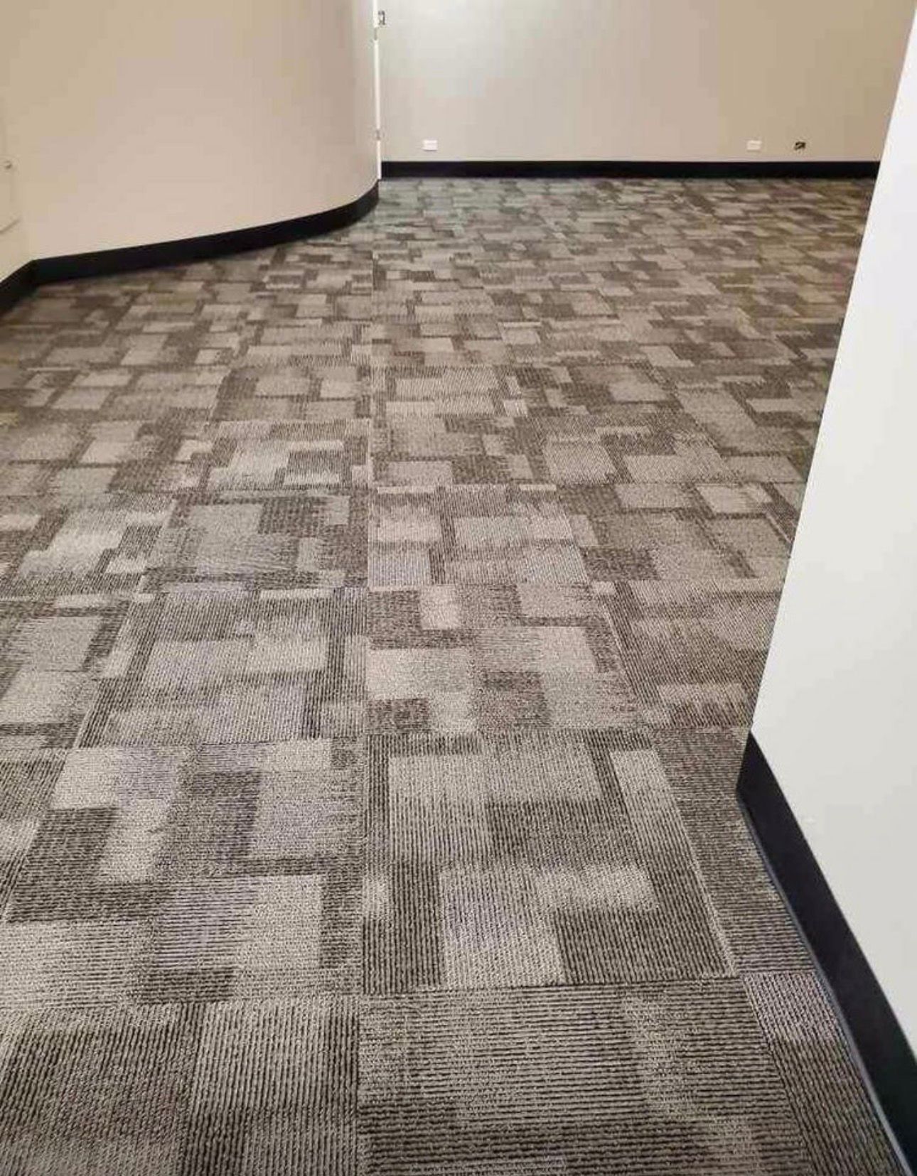 Empty hallway with gray patterned carpet, white walls, and black baseboards.