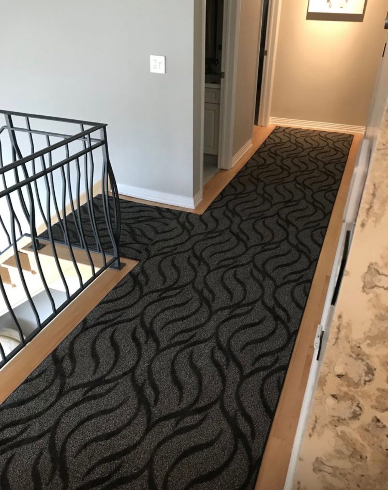 Narrow carpeted hallway with a dark swirling pattern, railing on the left and doorway at the end