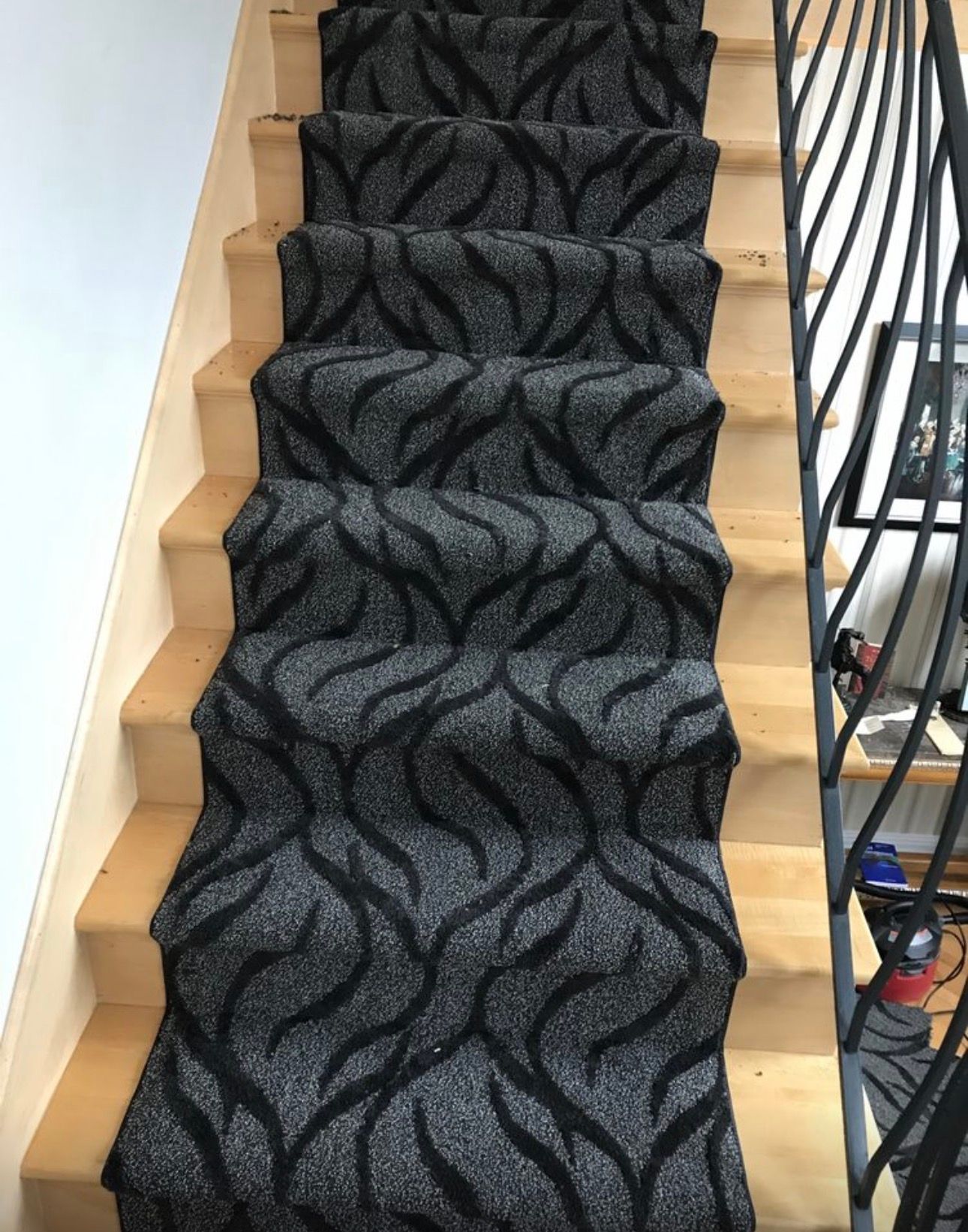 Carpeted staircase with dark patterned runner and a black railing on the right