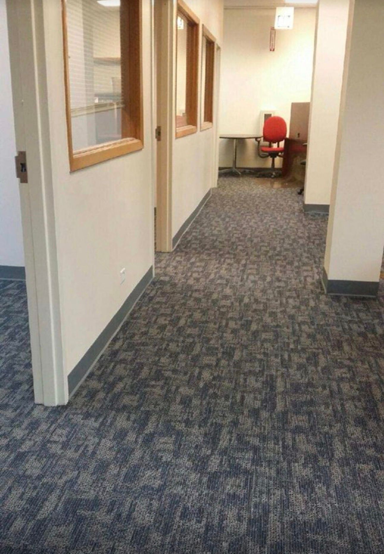 Office hallway with gray carpet, beige walls, and a red chair at the far end
