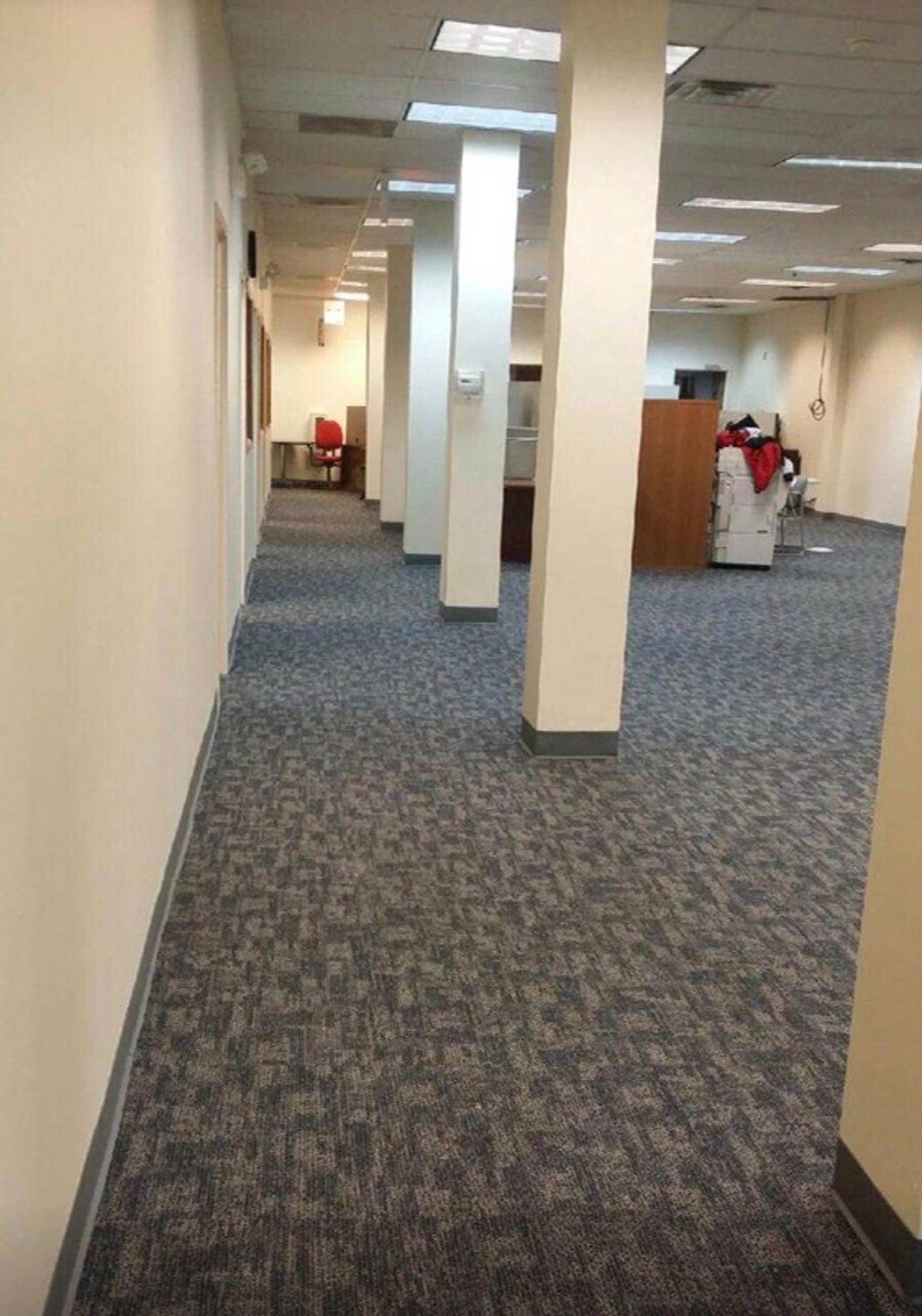 Empty office hallway with beige walls, blue-gray carpet, and rows of columns leading into the distance
