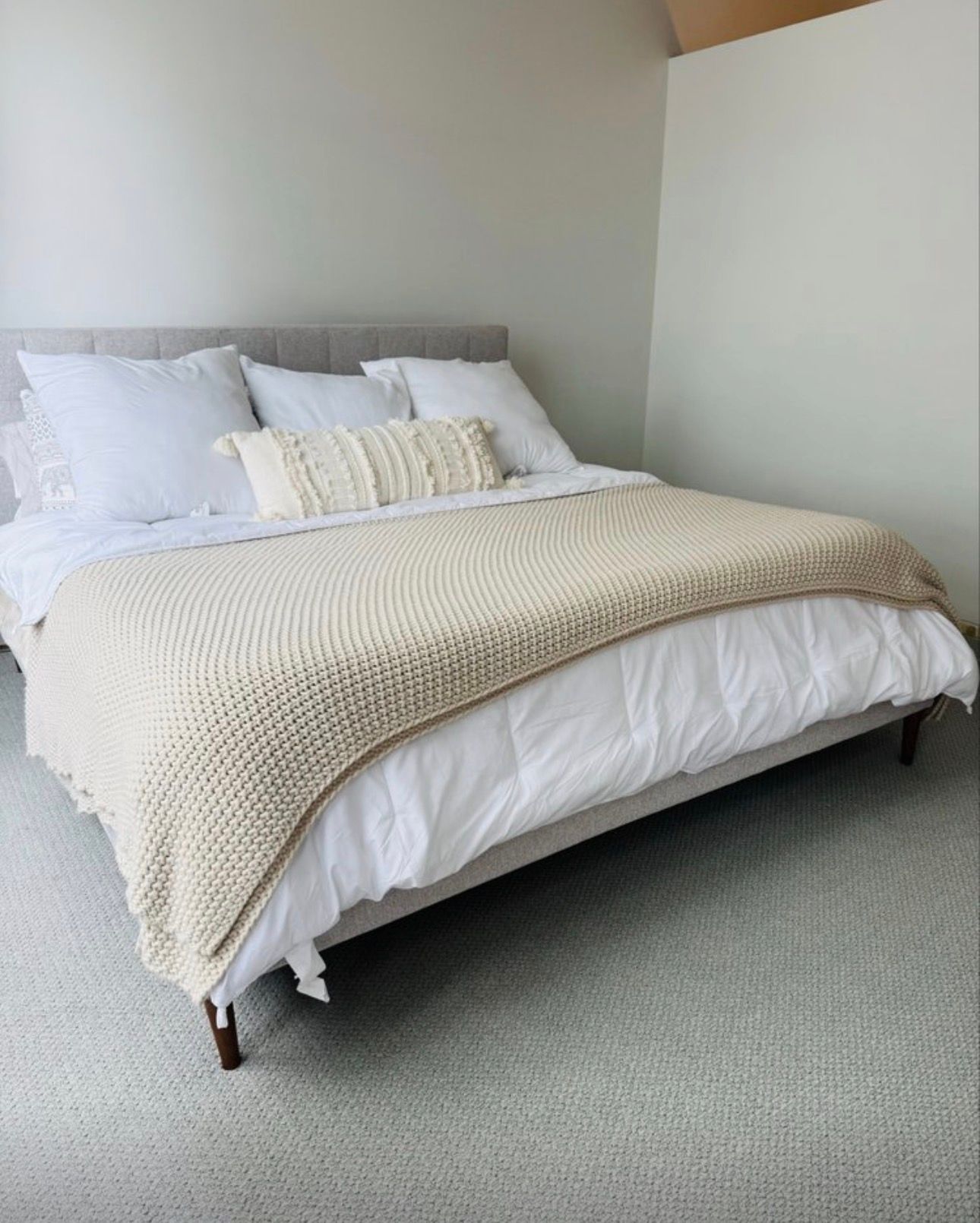Neatly made bed with white pillows and beige knit throw in a minimalist bedroom