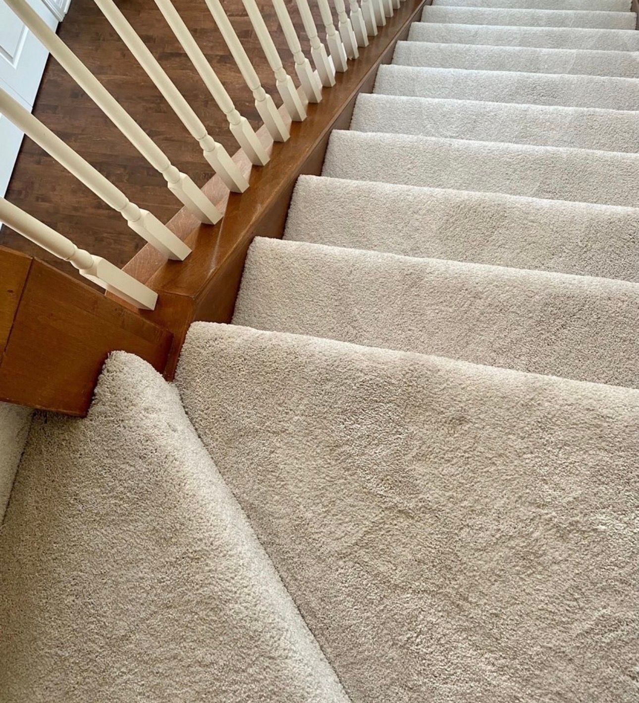 Carpeted staircase with white banister and wooden trim, viewed from above
