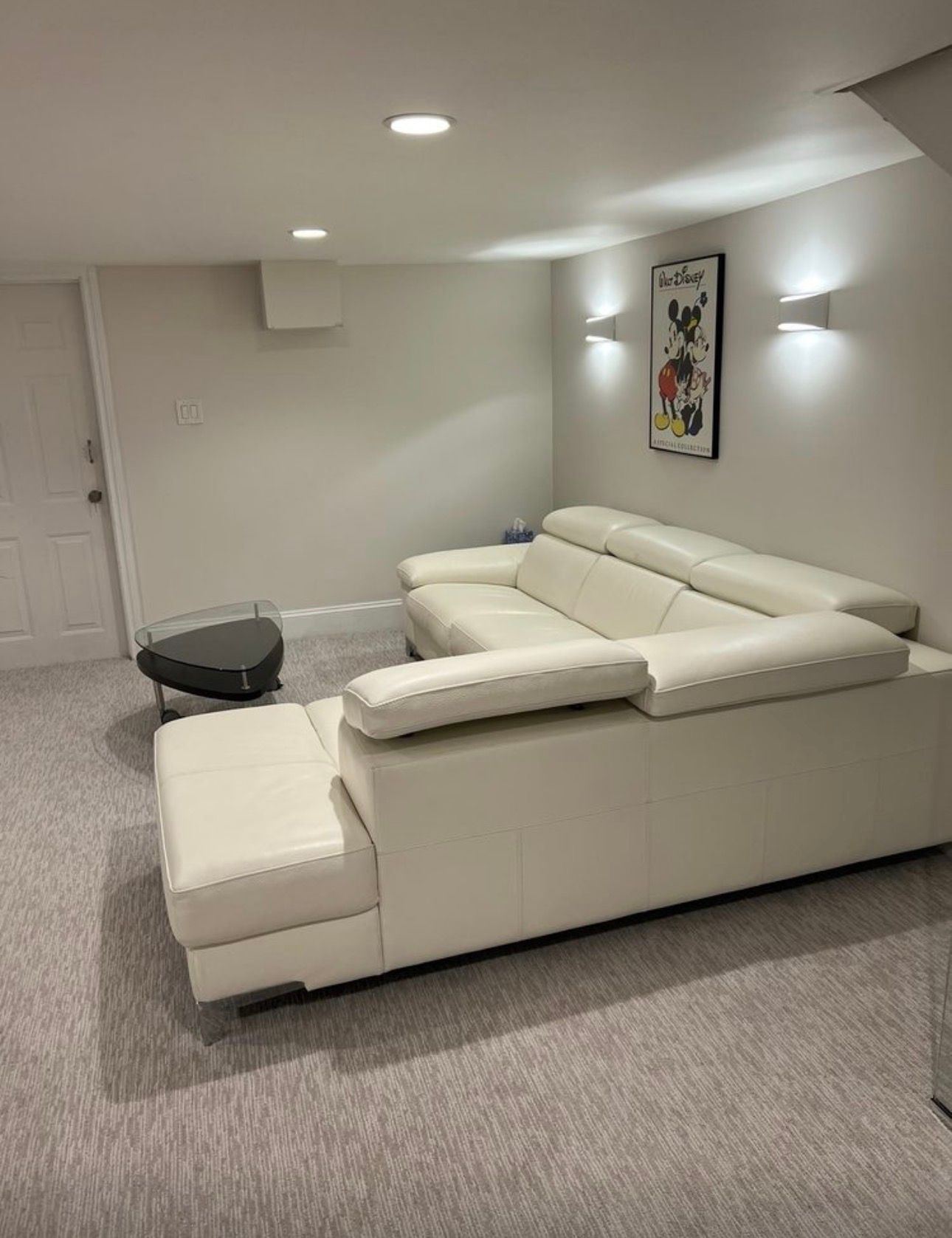 Modern living room with a white sectional sofa, black round table, beige carpet, and framed wall art.