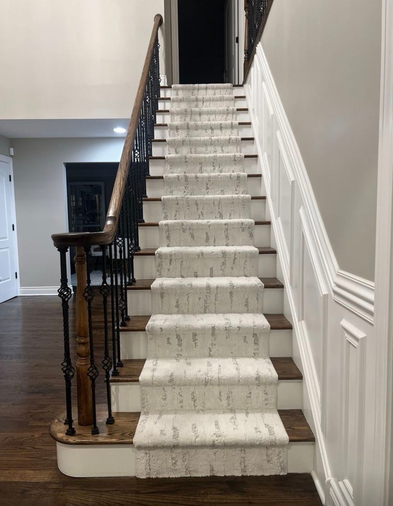 Carpeted staircase with dark wood and black iron railing in a white hallway