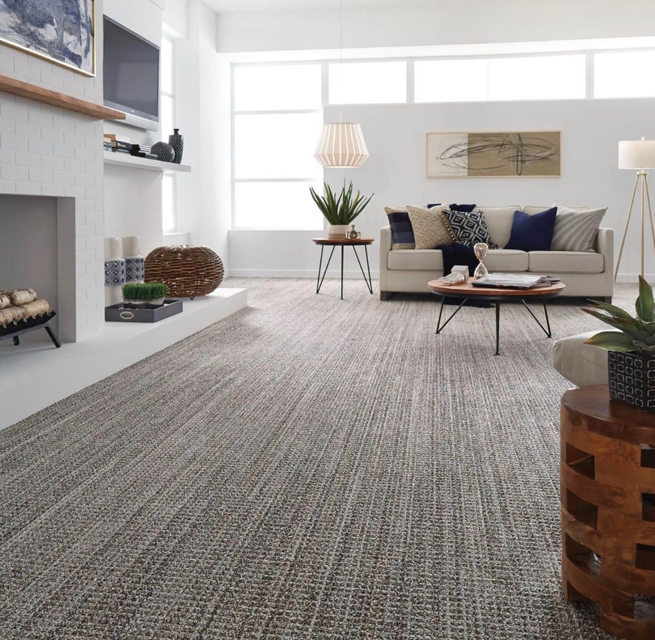Bright modern living room with a gray sectional, large rug, fireplace, and wooden coffee tables