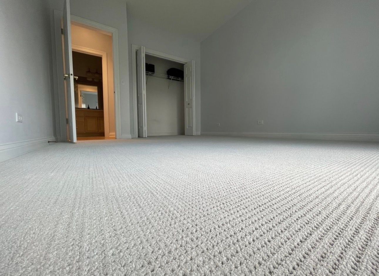 Empty gray-carpeted room with white walls and an open closet and doorway.