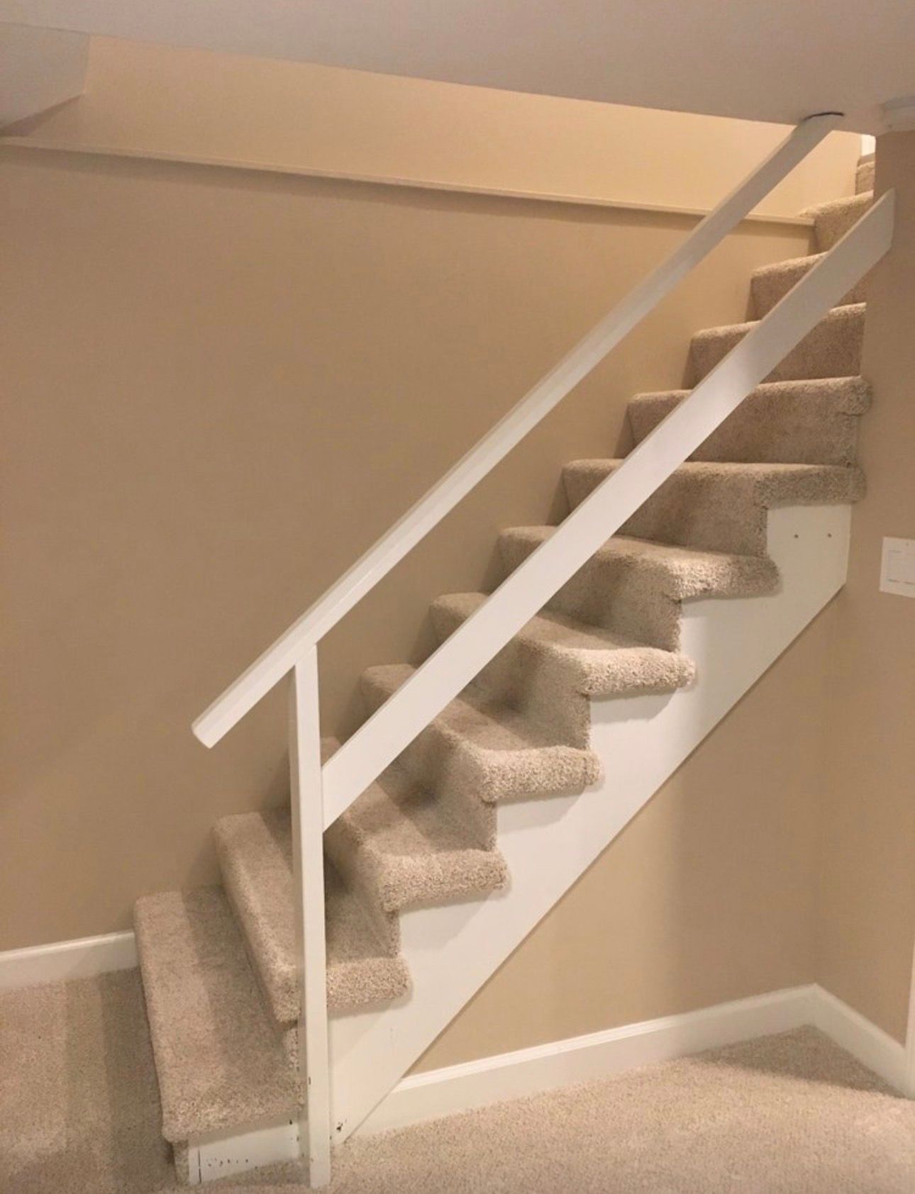 Carpeted staircase with white railing in a beige interior hallway