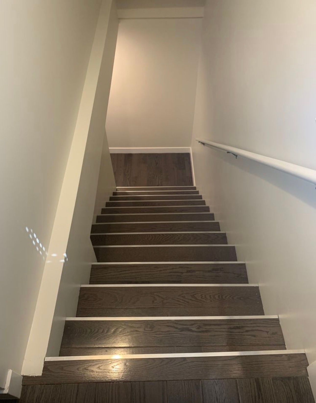 Narrow indoor staircase with dark carpeted steps, white walls, and a handrail on the right.