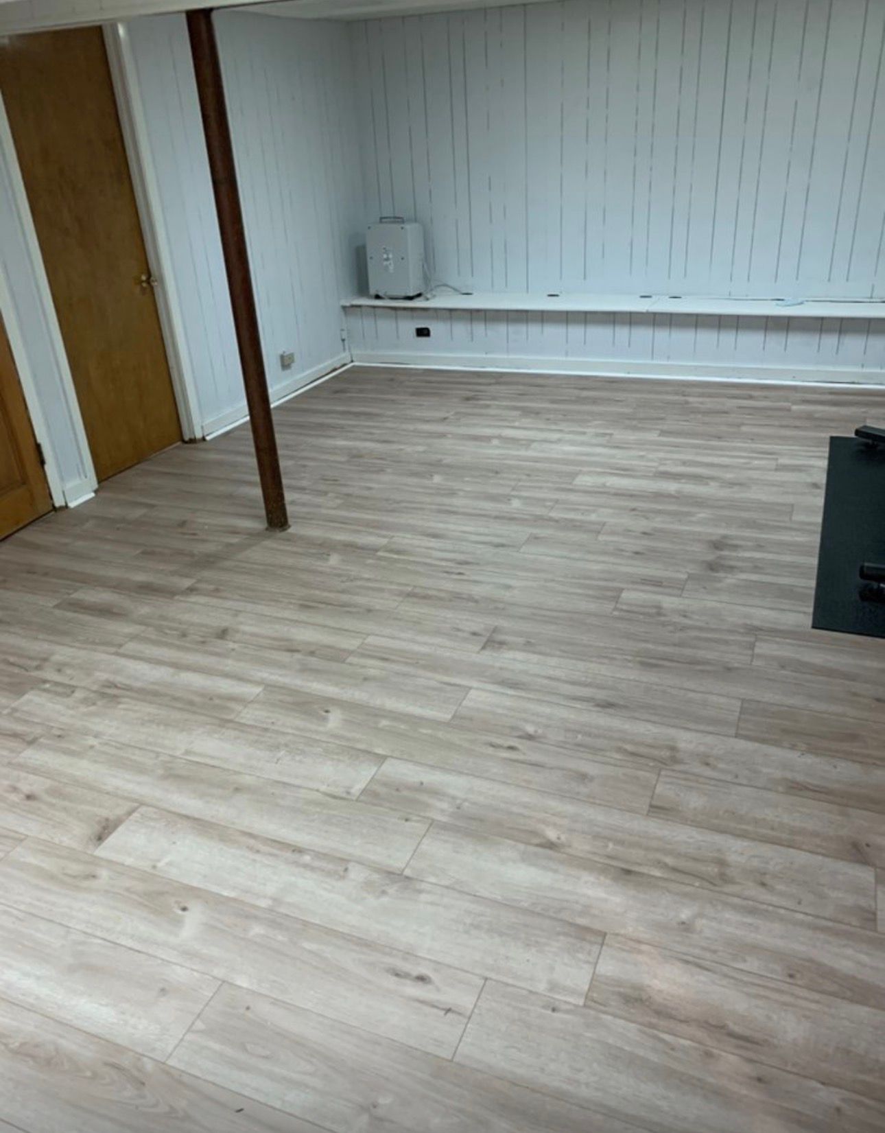 Empty room with light wood flooring, white paneled wall, and a small black stove in the corner