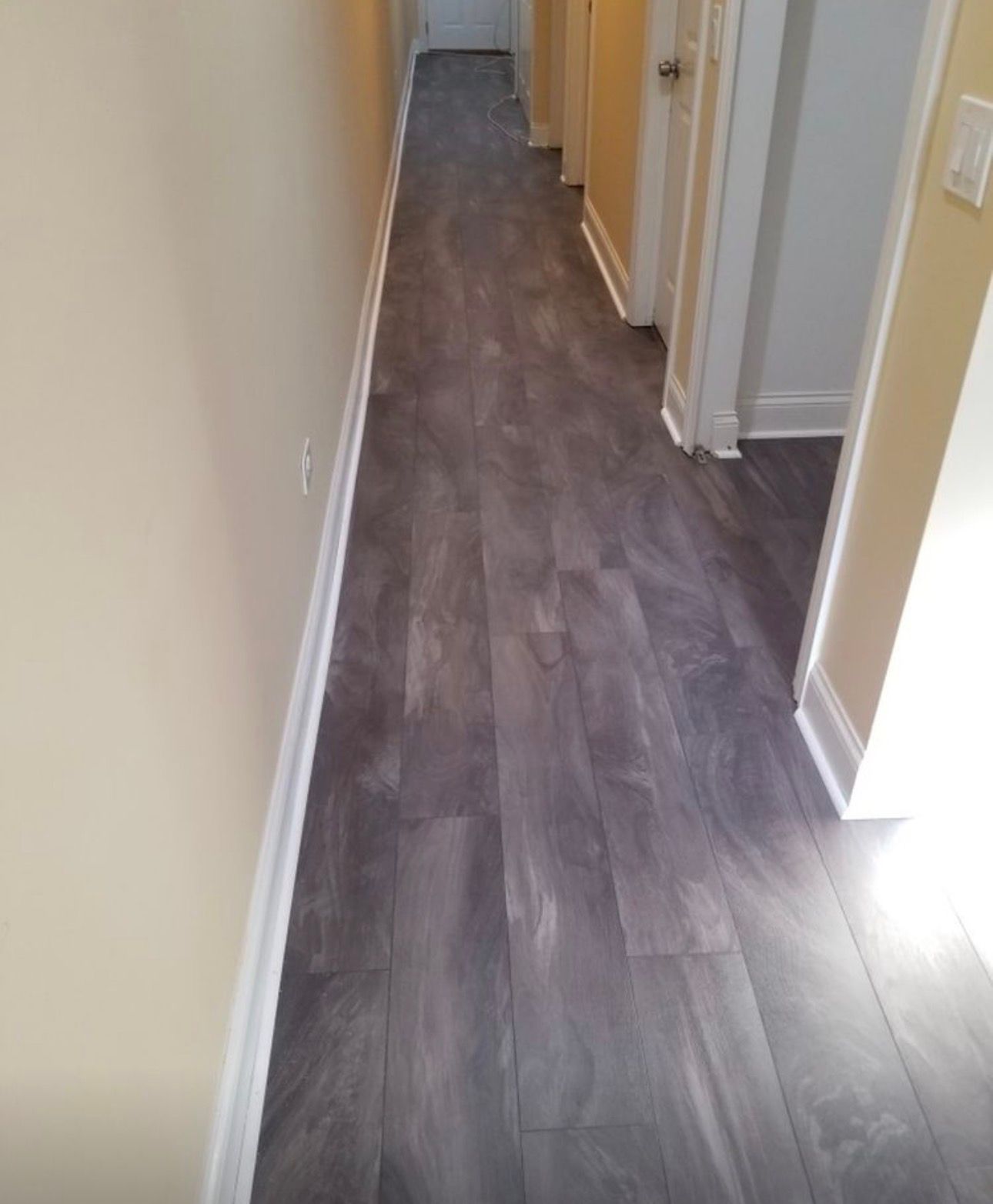 Narrow hallway with gray wood-look flooring and beige walls, viewed from one end.