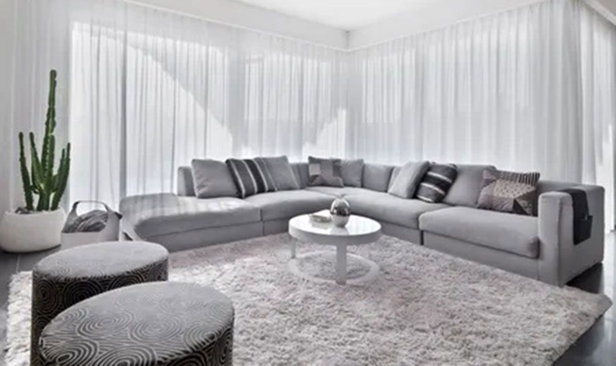 Bright modern living room with a curved gray sectional, shag rug, round coffee table, and sheer white curtains.