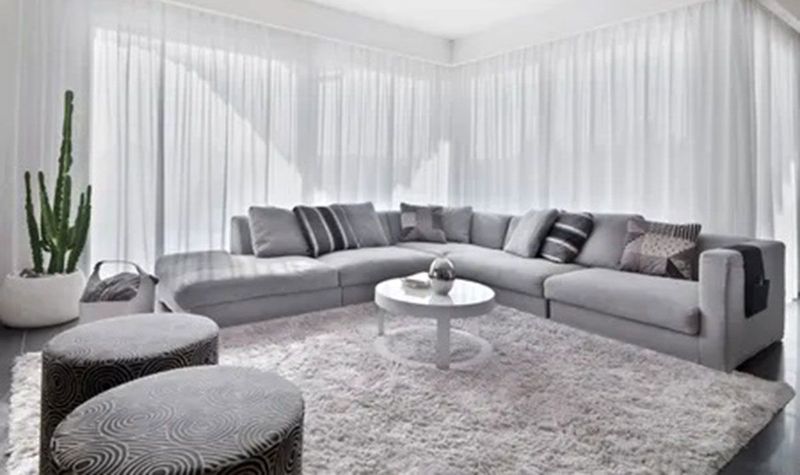 Bright modern living room with a curved gray sectional, shag rug, round coffee table, and sheer white curtains.