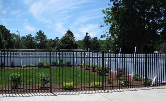 Black metal fence surrounds a small grassy area with landscaping under a blue sky.