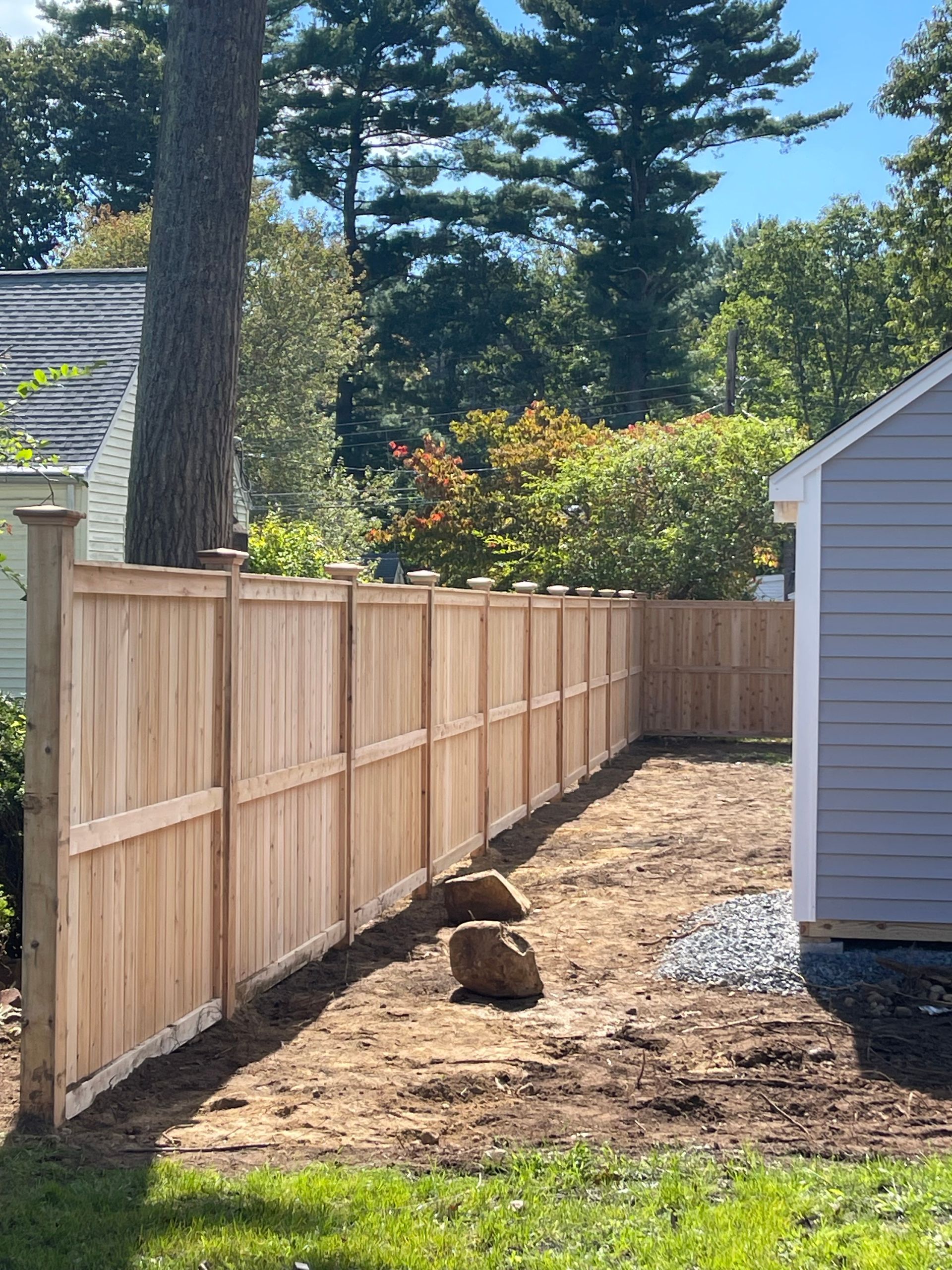 Wooden fence with posts, next to a light blue building and trees.