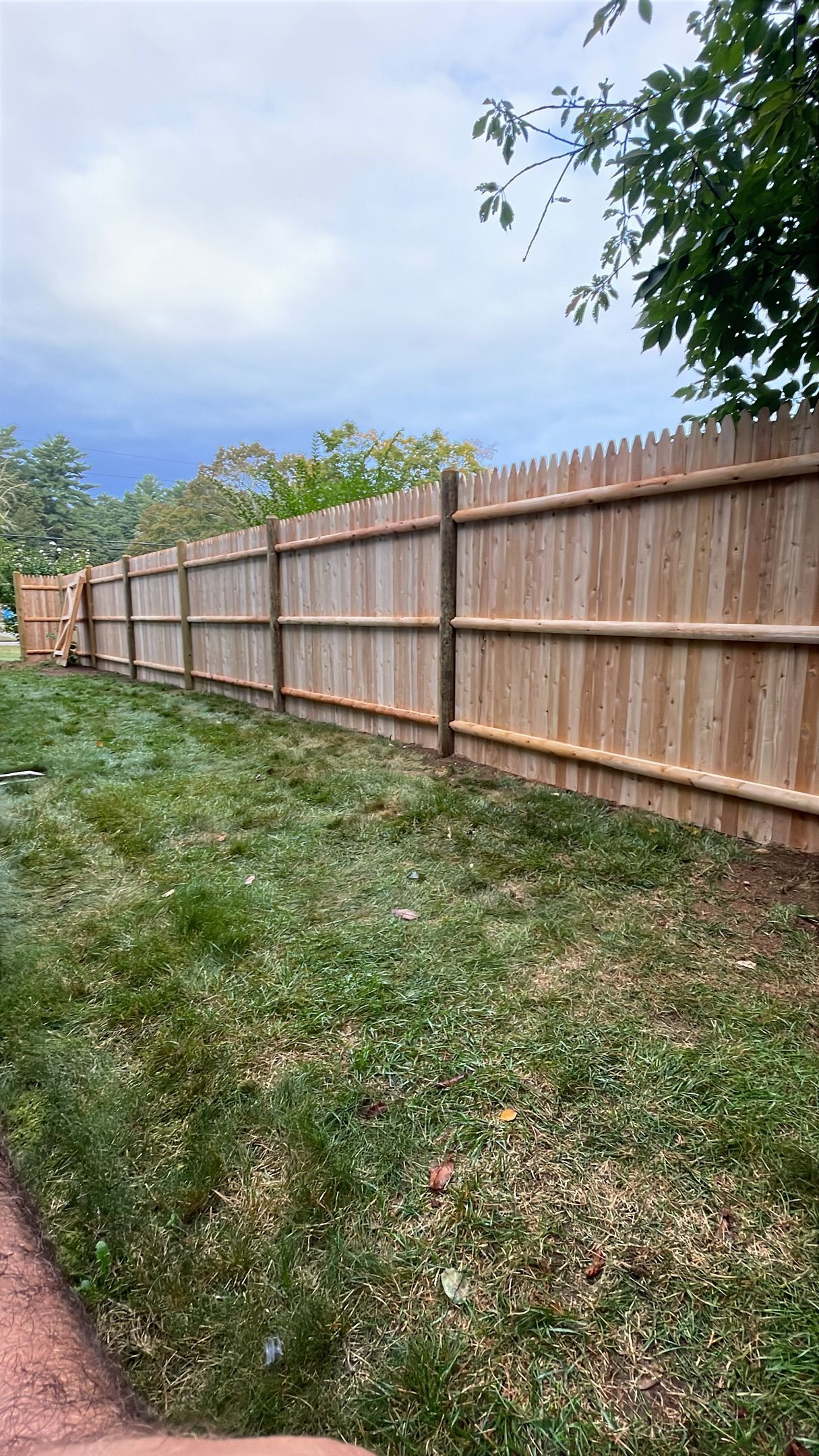 Wooden fence in a grassy yard under a cloudy sky.