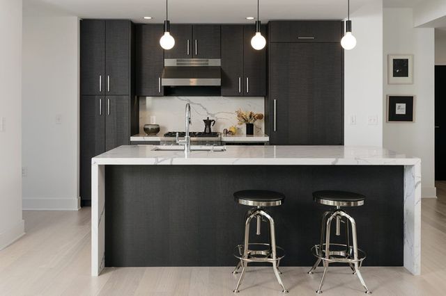 Modern kitchen with dark cabinets, white island countertop, and two bar stools under pendant lights