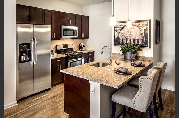 Modern kitchen with stainless steel appliances, dark wood cabinets, and a granite island with two bar stools