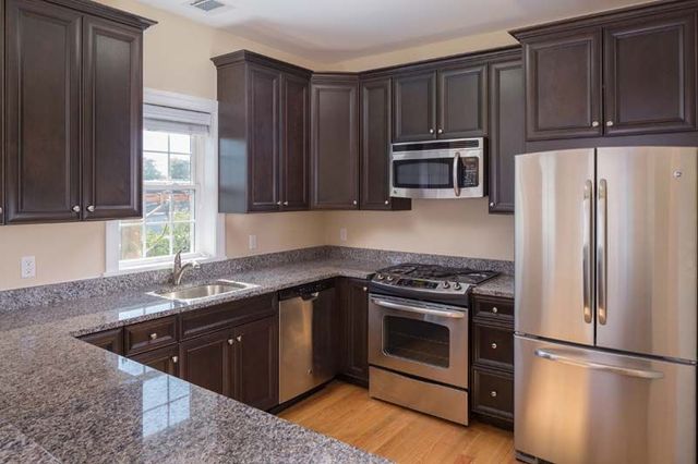 Modern kitchen with dark wood cabinets, granite counters, stainless steel appliances, and a window over the sink