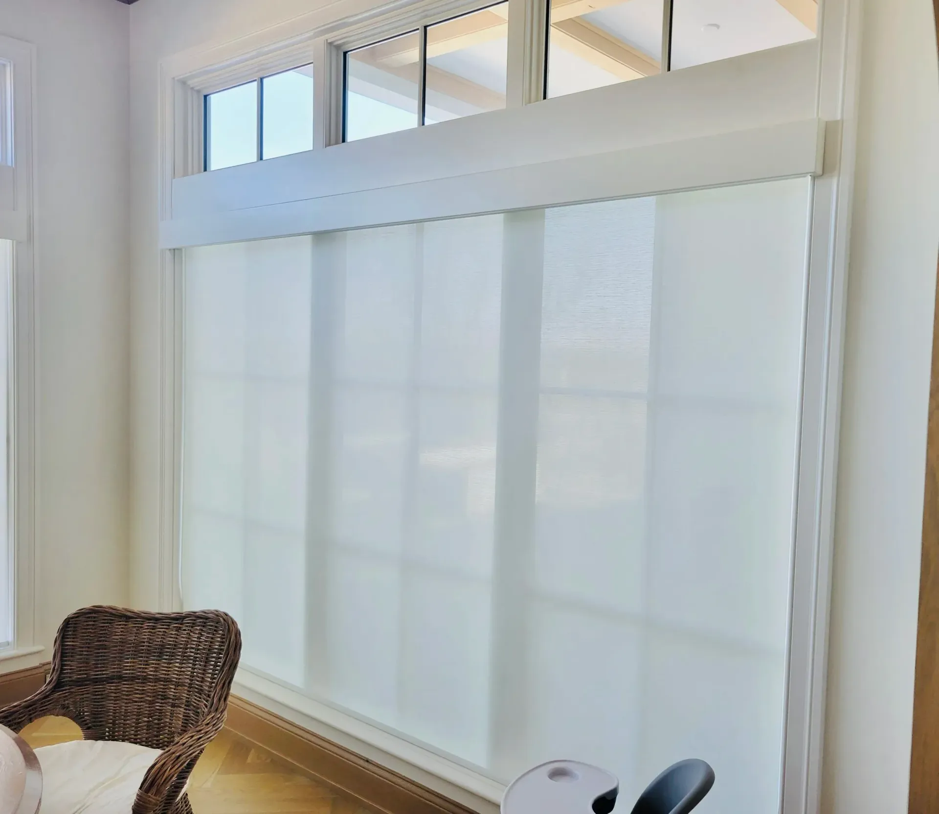 Large white window blinds cover a window; a wicker chair is visible on the left.