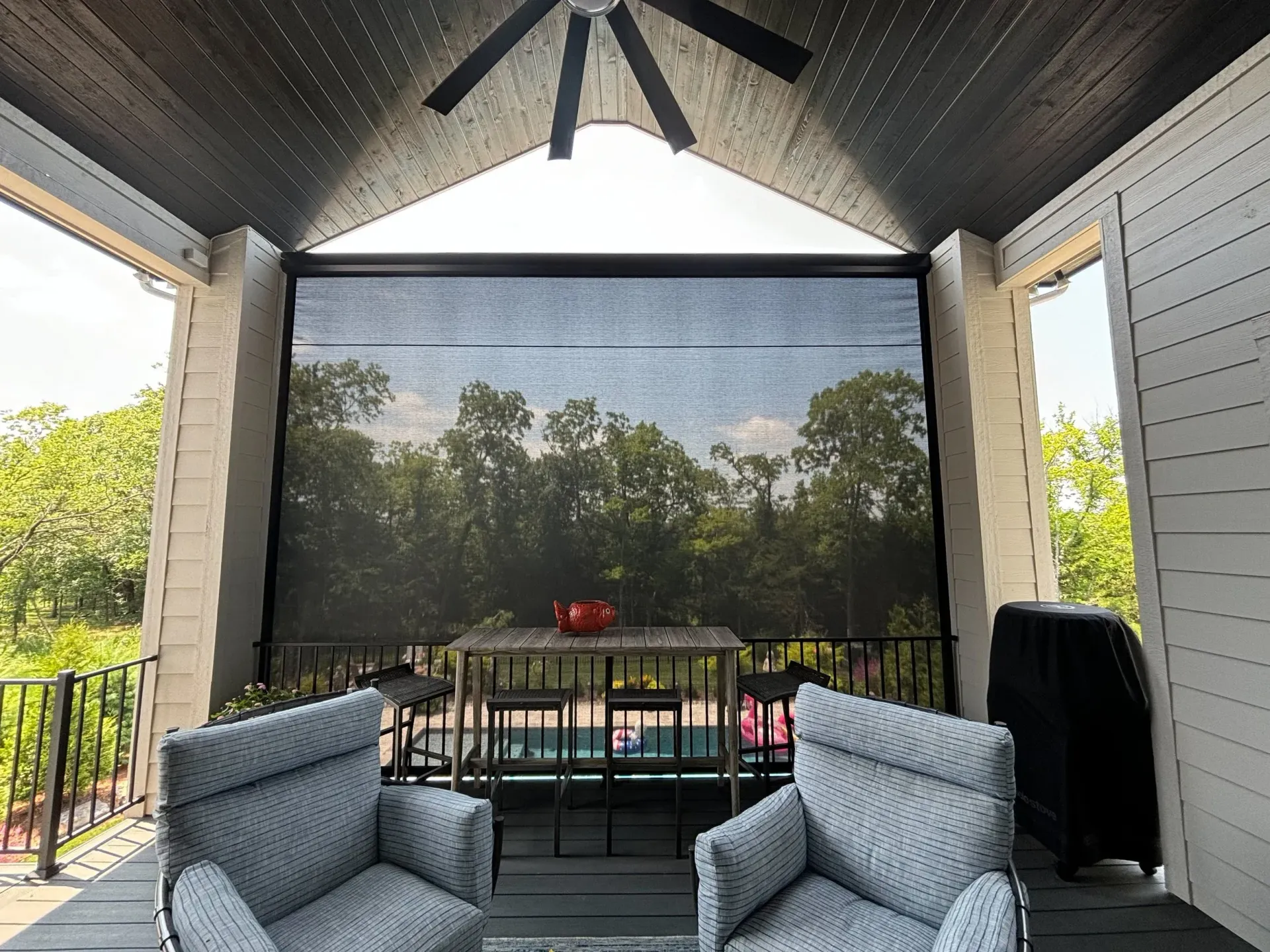 Covered patio with retractable shade, furniture, and a view of trees.