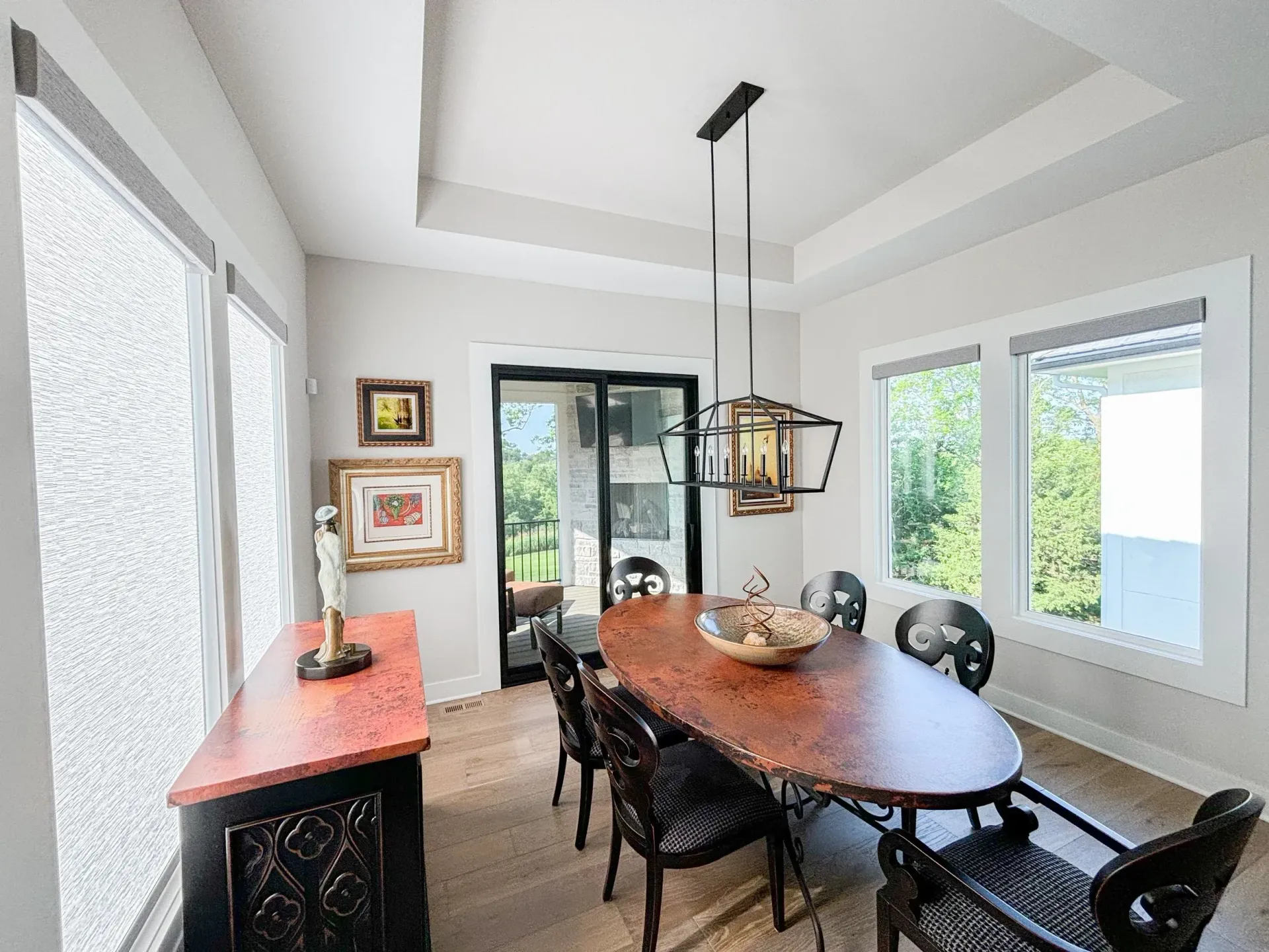 Formal dining room with oval table, chairs, and hanging light fixture. Windows and sideboard along the walls.