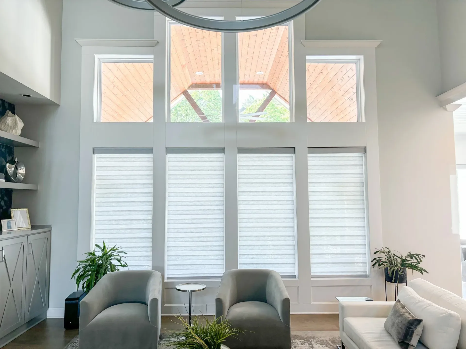 Living room with large windows, light gray walls, two armchairs, a couch, and built-in shelves.