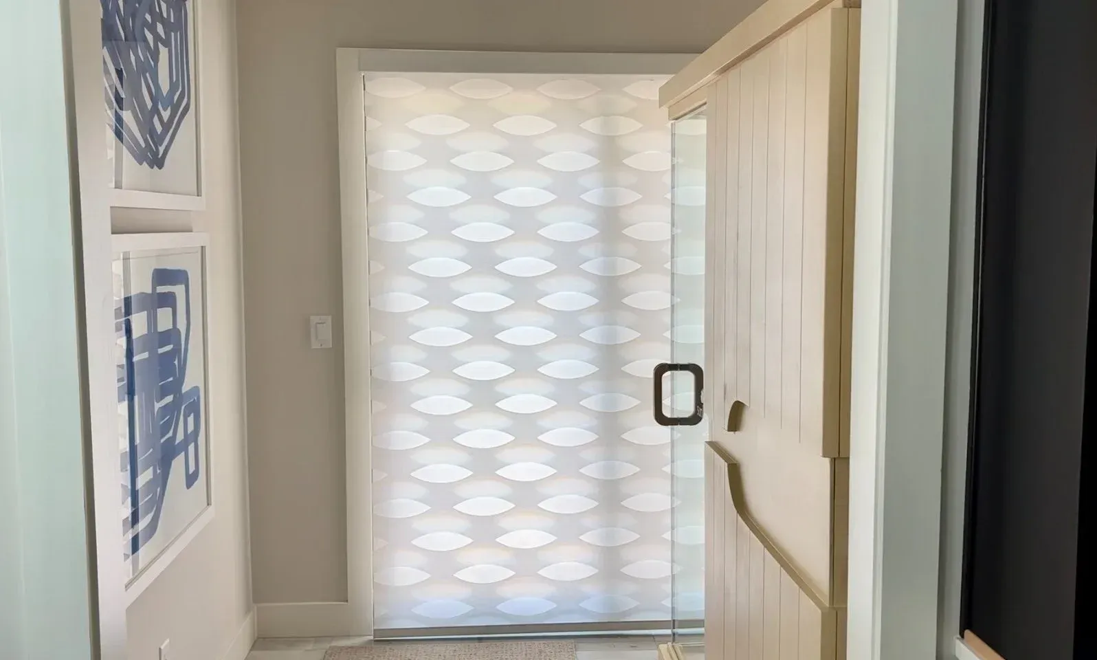 Hallway with a patterned shade, light wooden door, and blue artwork.