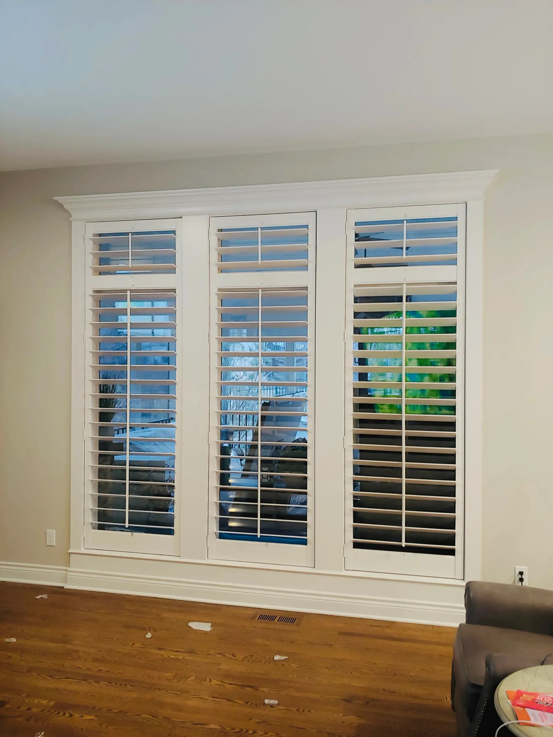 Three white paneled windows with adjustable shutters in a room with hardwood floors and light gray walls.