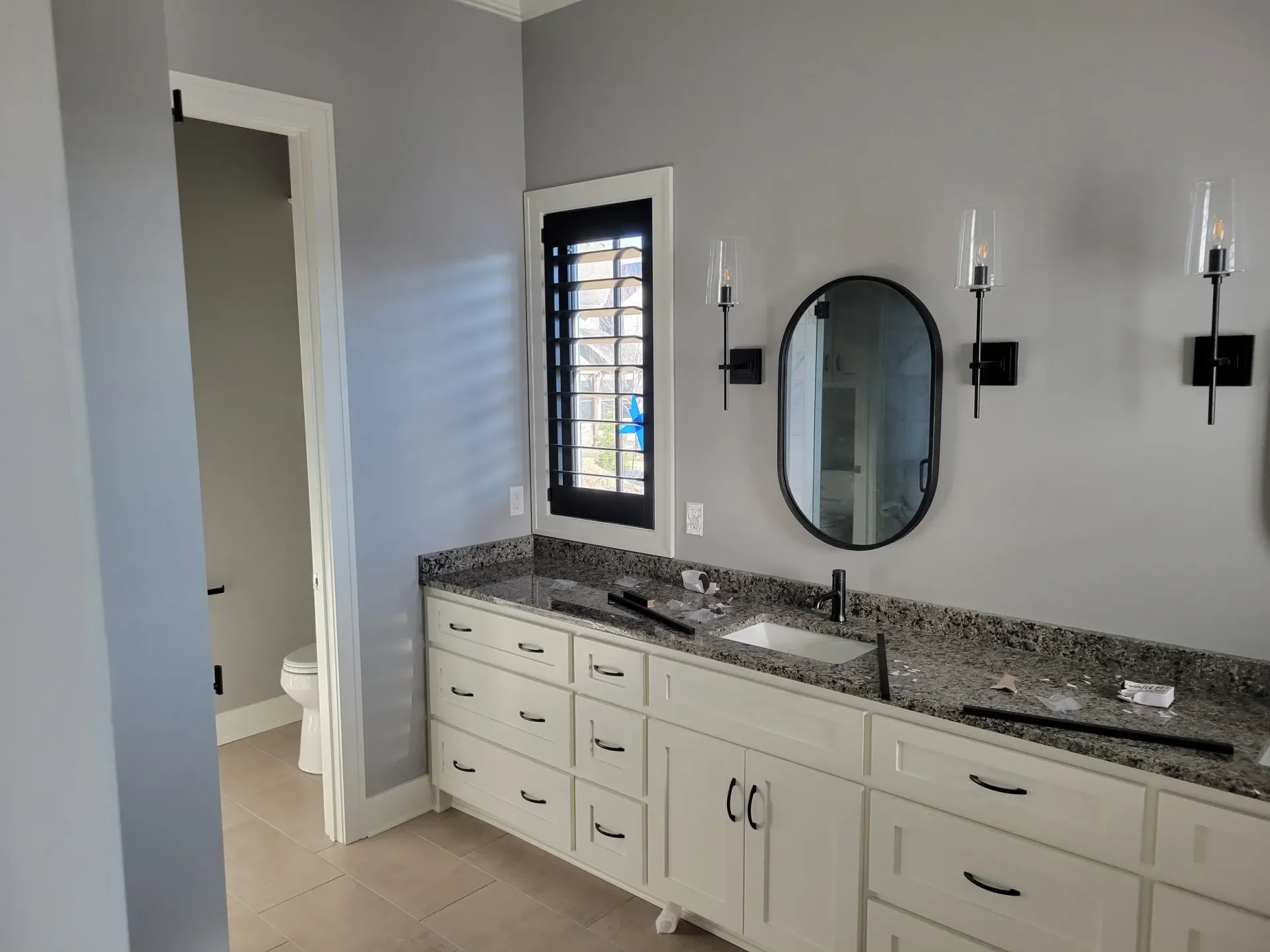 Bathroom with white cabinets, gray walls, and a black-framed mirror.