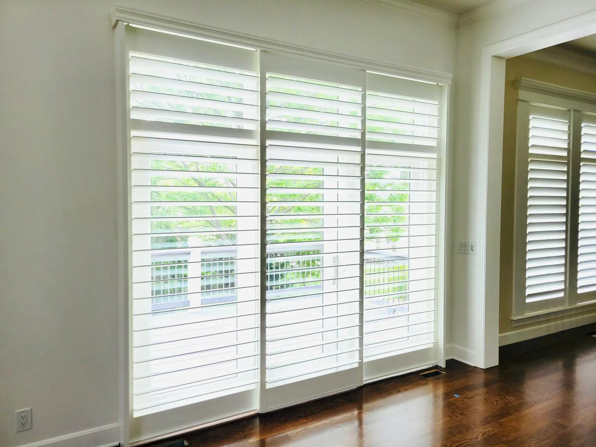 Three white shuttered sliding doors in a bright room with dark wood floors.