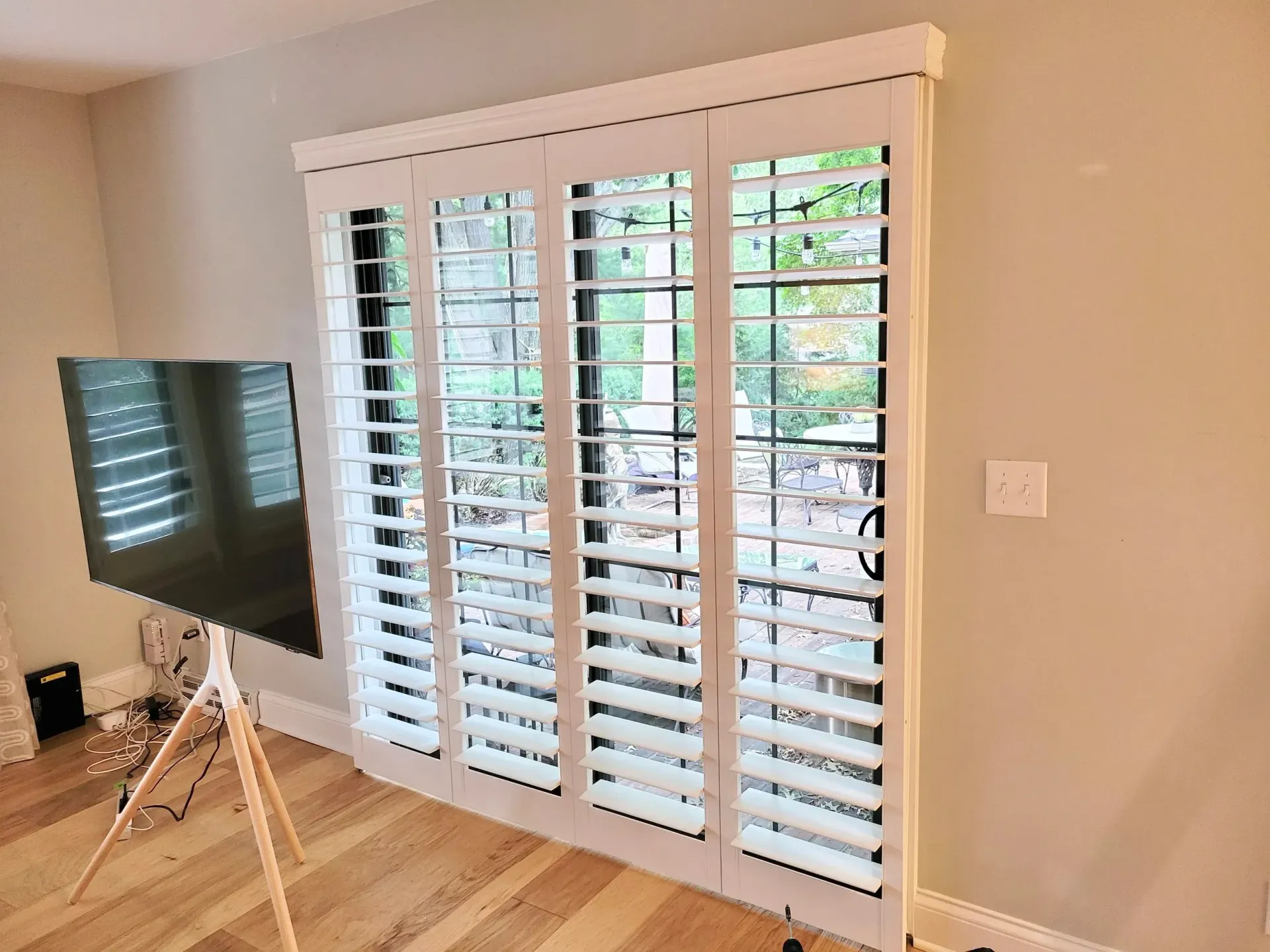 White shutters cover windows. A TV is on a stand in front of the window.