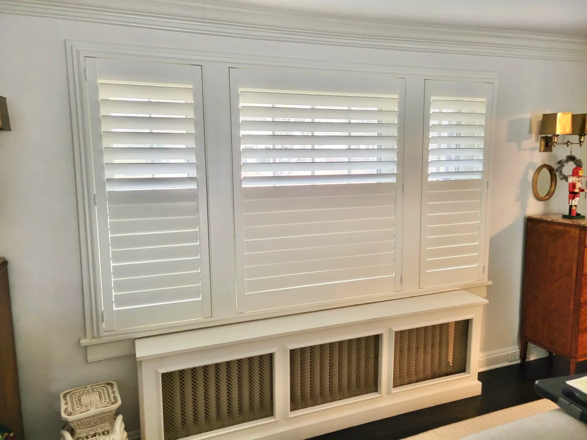 White shutters cover a window above a radiator, with ornate trim and a cabinet visible.