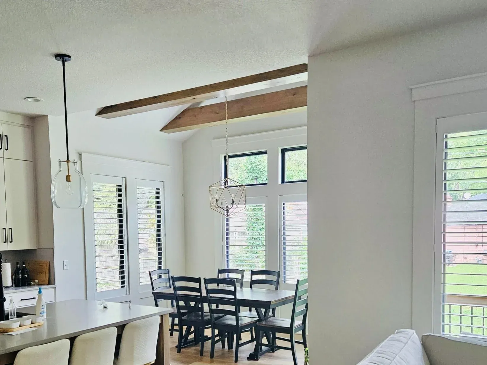 Dining room with table and chairs, large windows, wood beams, and white walls.
