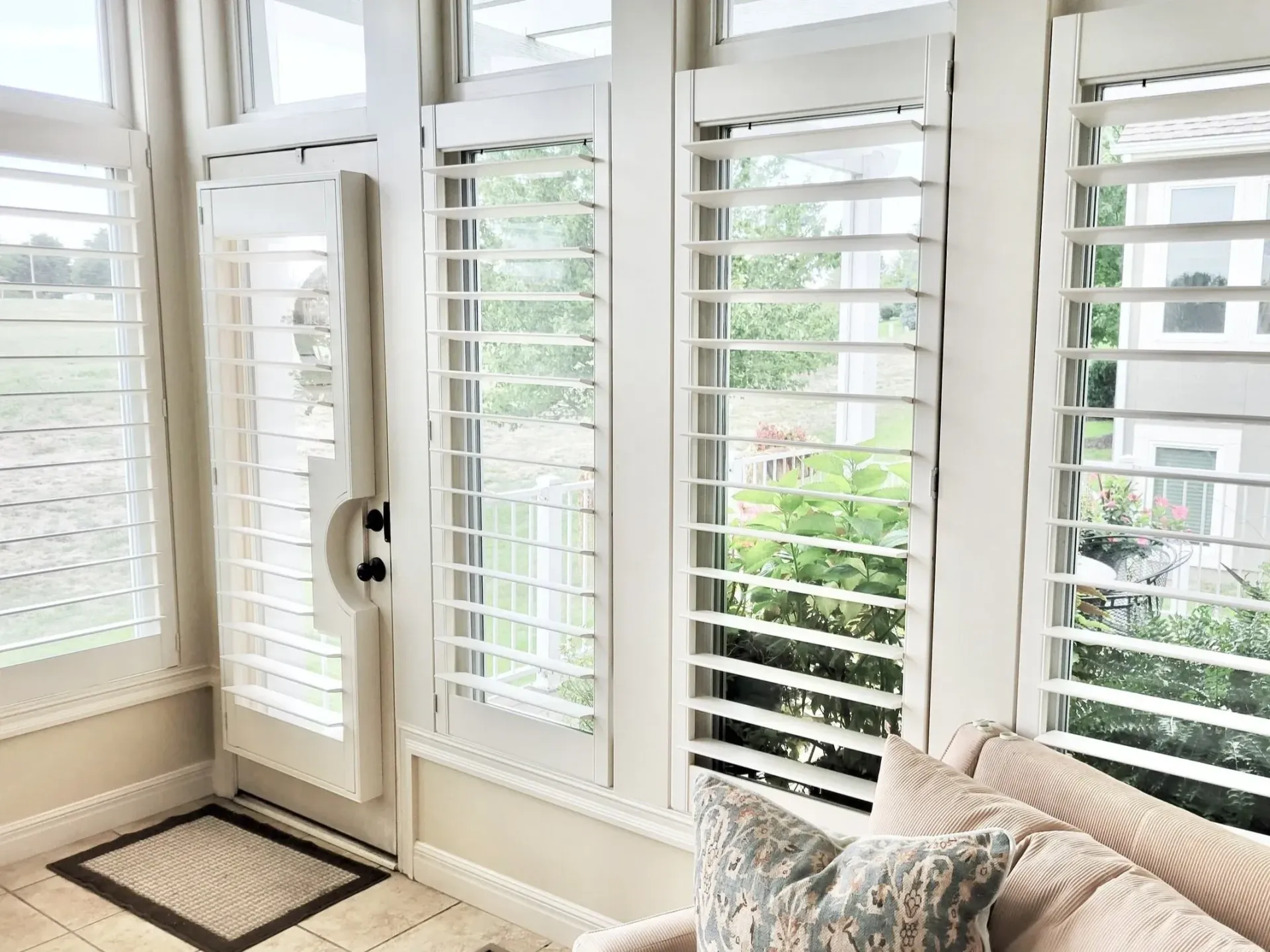 White shutters on a sunroom with outdoor view, beige walls, and light fixture.