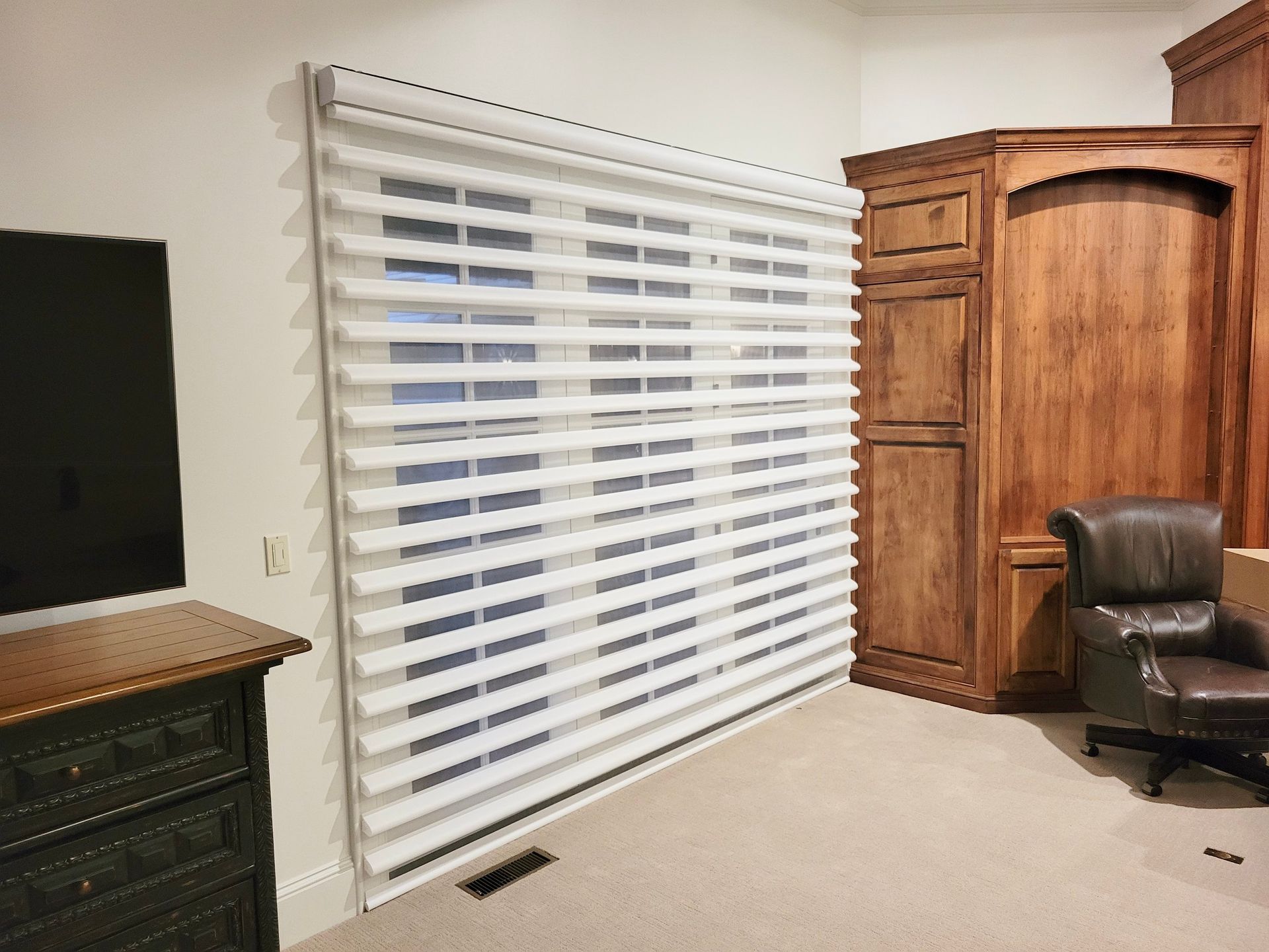 Room with sheer horizontal blinds covering a window; a dark wooden dresser and cabinet on either side.